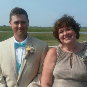 son in suit, siting with mom in gold dress at wedding, both smiling, best friends