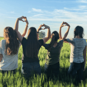 4 girls in field forming hearts with their hands