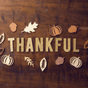 thankful written on wood table with fall leaves scattered