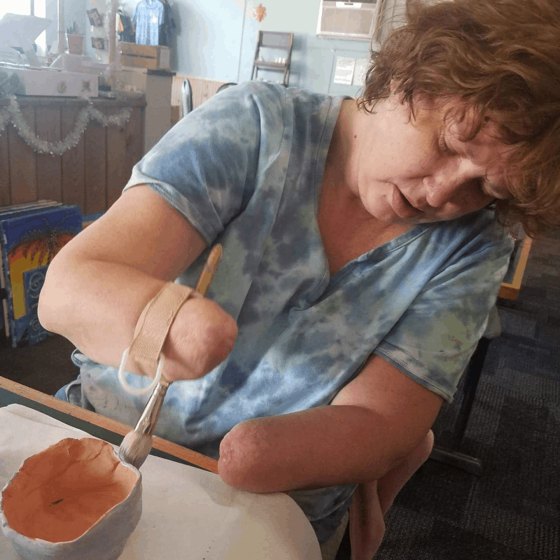 Amputee woman painting clay bowl