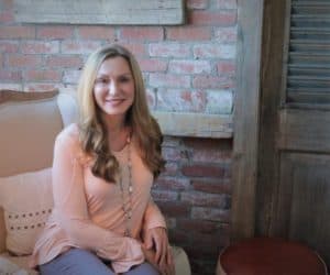 pretty blonde woman, pink sweater sitting in front of brick wall