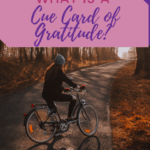woman riding bike on fall colored road, cue card of gratitude