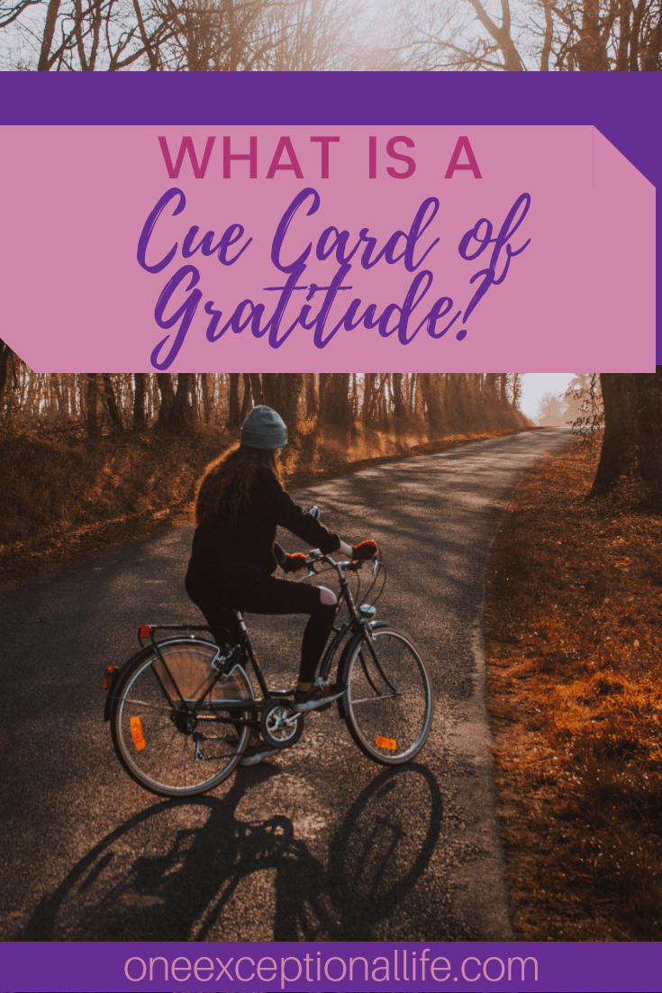 woman riding bike on fall colored road, cue card of gratitude
