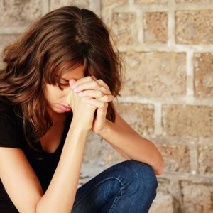 brunette woman in black tshirt hands clasped and head bowed in prayer