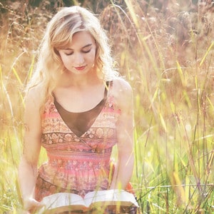 blonde woman reading bible while sitting in field
