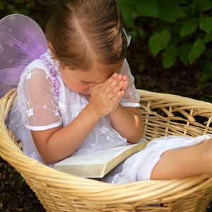 Little girl sitting in a basket in a dress while praying 